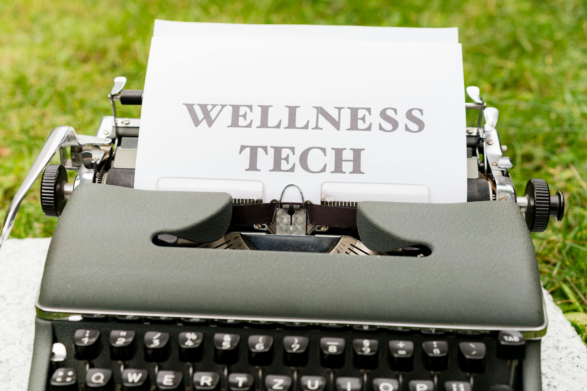 A retro typewriter outdoors displaying a 'Wellness Tech' message on paper.